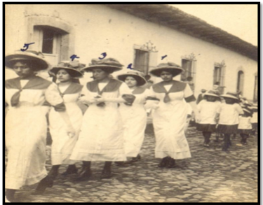 Estudiantes bien ataviadas, desfilan por las calles de Tegucigalpa en un desfile cívico. Numerada con el 3, la estudiante María Prica Zúñiga Huete y numerada con el 4, Graciela Bográn, 1913. Archivo personal de José Gonzáles. 