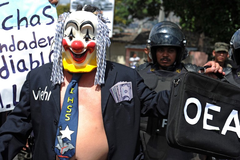 A man with a clown mask and a tie reading "IHSS", referring to the Honduran Institute of Social Security takes part in a protest of the National Front of Popular Resistance (FNRP) during the celebration of the 194th anniversary of the Honduran independence in Tegucigalpa, on September 15, 2015. The FNRP demands the resignation of Honduran President Juan Orlando Hernandez and the installation of an International Commission Against Impunity (CICIH) in the country. AFP PHOTO/Orlando SIERRA
