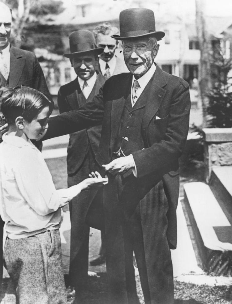John D. Rockefeller da monedas a un niño frente a los reflectores locales. Fuente: The Daily News